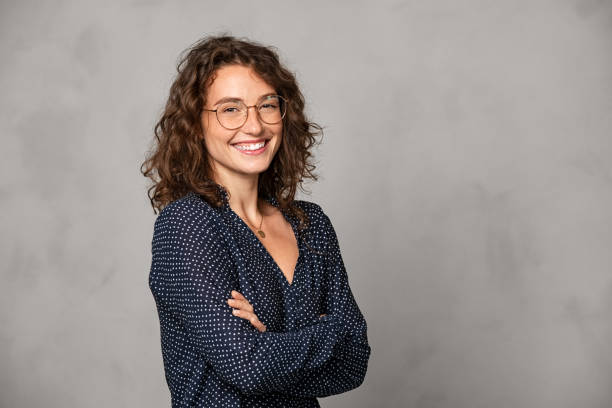 mujer sonriente exitosa con gafas en la pared gris - experto fotografías e imágenes de stock
