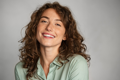 Close up face of beautiful young woman smiling and looking at camera isolated on grey background. Portrait of beauty natural girl with copy space. University female student in casual standing against gray background.