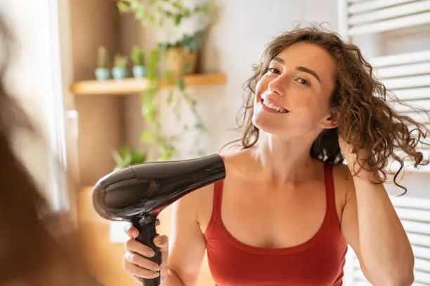 Photo of Happy smiling woman using hair dryer in bathroom