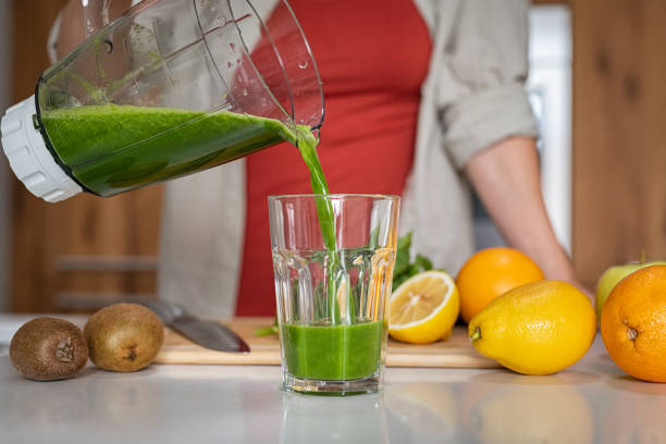 fille versant le jus fait main vert dans le verre - green smoothie smoothie nutritional supplement leaf vegetable photos et images de collection