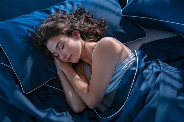 Young woman sleeping profoundly at night Top view of young beautiful woman dreaming in bed and relaxing at night. High angle view of woman with closed eyes sleeping well at home in the dark. Beautiful girl sleeping peacefully under blue blanket in her bedroom at late in night. bedtime stock pictures, royalty-free photos & images