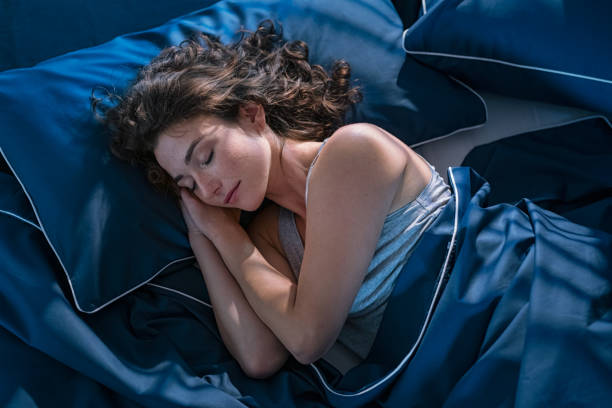 Young woman sleeping profoundly at night Top view of young beautiful woman dreaming in bed and relaxing at night. High angle view of woman with closed eyes sleeping well at home in the dark. Beautiful girl sleeping peacefully under blue blanket in her bedroom at late in night. lying on side stock pictures, royalty-free photos & images