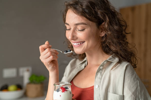 donna che mangia yogurt con bacche a casa - yogurt yogurt container strawberry spoon foto e immagini stock