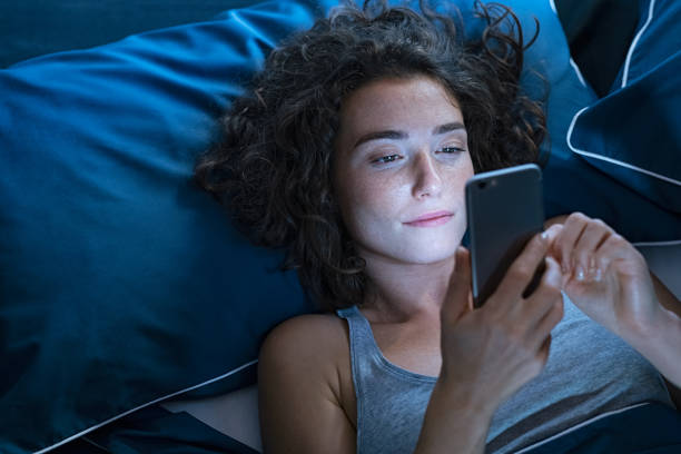 meisje dat in bed wordt wakker gebruikend cellphone bij nacht - bed stockfoto's en -beelden