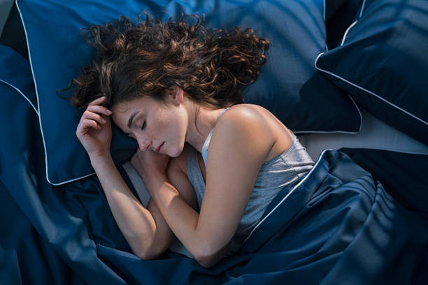 Young woman sleeping in bed at night Top view of young woman sleeping on side in her bed at night. Beautiful girl sleeping profoundly and dreaming at home with blue blanket. High angle view of woman asleep with closed eyes. bedtime photos stock pictures, royalty-free photos & images