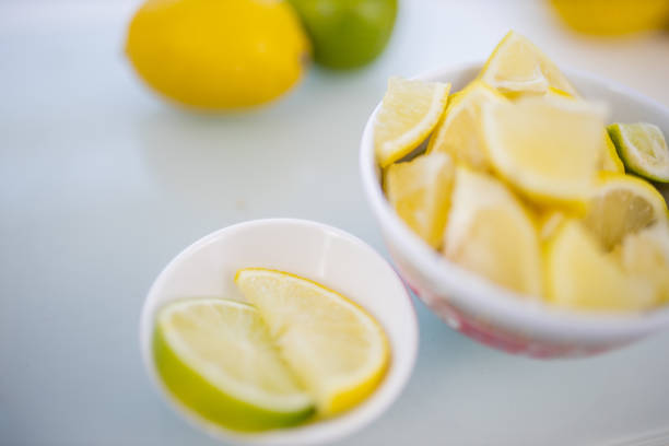 Bowls of limes and lemons slices and on table with limes and lemons as background. Fruit slices on transparent cutting board. Sweet and healthy snacks