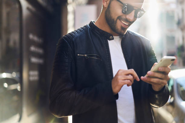 istock Crop happy ethnic man chatting via smartphone while standing outside modern building 1289223760
