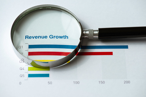 Revenue-Growth chart on printed paper with a magnifying glass on white background.