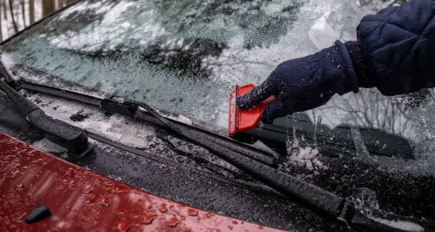 Photo of Hand Close Up cleaning the ice down the windshield from the snowy car
