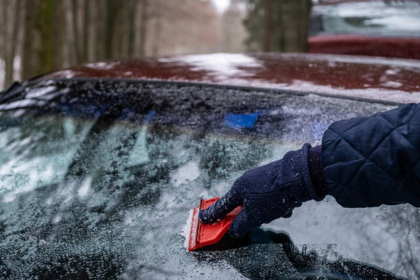 istock Hand Close Up cleaning the ice down the windshield from the snowy car 1289226283