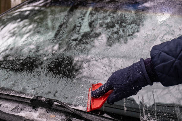 istock Hand Close Up cleaning the ice down the windshield from the snowy car 1289226409