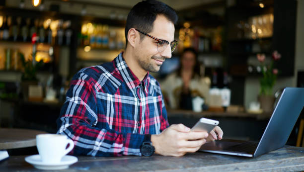 istock Delight brunette man using laptop and cellphone in modern cafe 1289226520