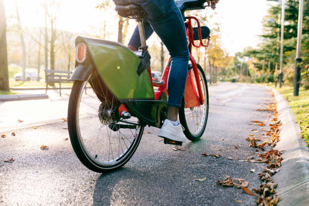 fotografia posteriore di un ragazzo studente con una borsa sulla schiena che trasporta una bici elettrica condivisa rossa lungo un percorso del parco alberato al tramonto - bicicletta elettrica foto e immagini stock