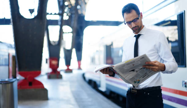 istock Focused young man reading newspaper on platform of railway station 1289226567
