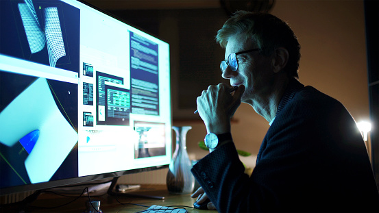Close up stock photograph of a mature man working with a large computer screen. He’s working with 3D software examining complicated shapes.
