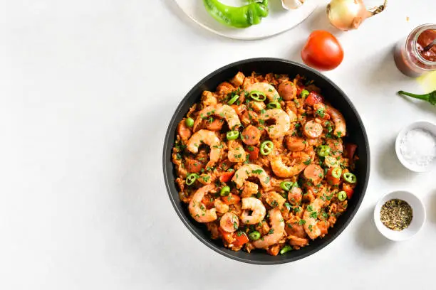 Creole jambalaya with chicken, smoked sausages and vegetables in frying pan on white stone background with copy space. Top view, flat lay, close up
