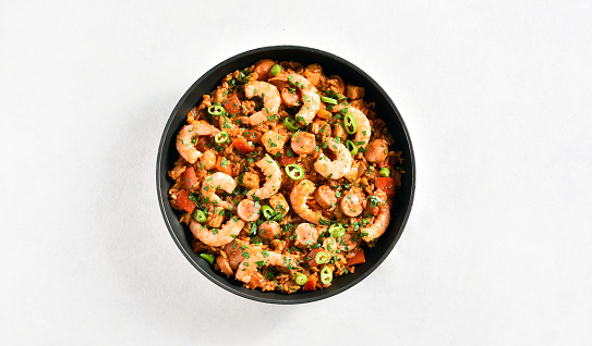 Creole jambalaya with rice, chicken, smoked sausages and vegetables in pan on white stone background with copy space. Top view, flat lay, close up