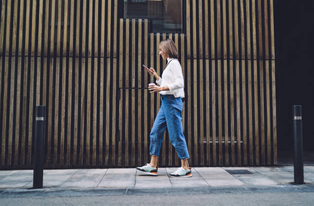Focused woman strolling on sidewalk and reading message on smartphone
