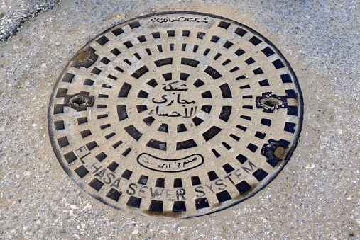 Al-Qarah, Al-Hofuf, Al-Ahsa Oasis, Eastern Province, Saudi Arabia: pavement with sewer manhole - the lid has text in English and Arabic. El Hasa sewer system.