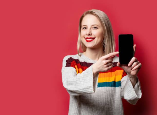 istock Beautiful blonde in sweater with mobile phone on red background 1289237486