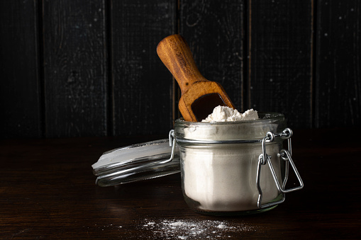 A glass jar with flour and a wooden scoop on an old rustic table.