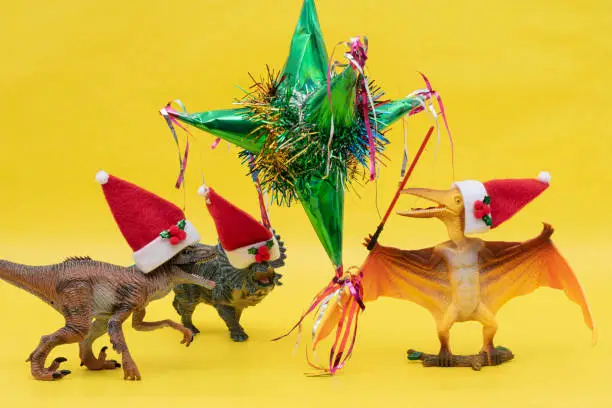 Photo of Three toy dinosaurs with Santa Claus hats and a mexican pinata