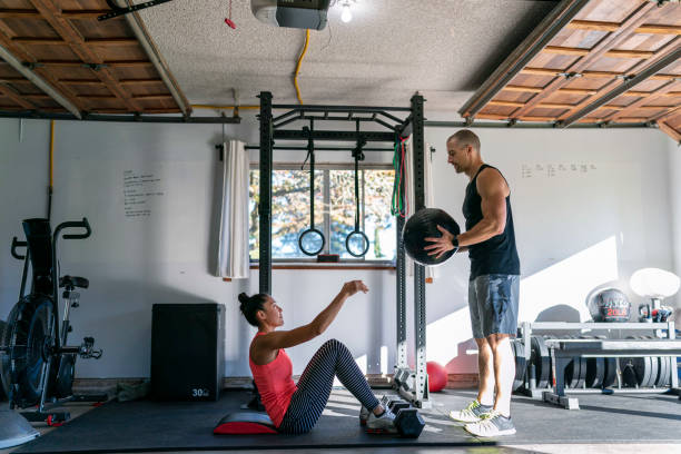 femme exerçant avec l’entraîneur personnel dans la gymnastique à la maison - muscular build wellbeing exercise equipment instructor photos et images de collection