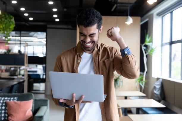 istock Cheering mixed race businessman using laptop during video call in office 1289248049