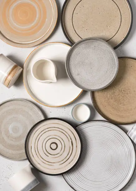 Top view of handmade ceramics, empty craft ceramic plates and cups on light background.