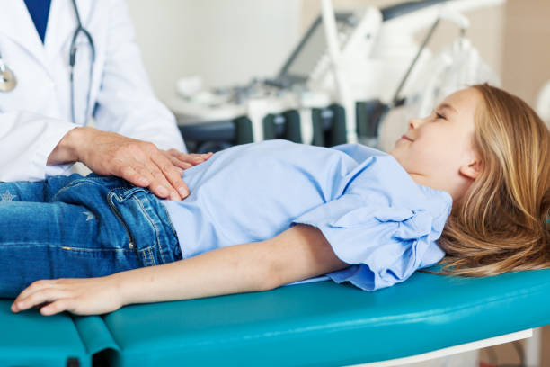 Unrecognizable doctor palpating belly of little girl lying on couch in doctors office and smiling Unrecognizable doctor palpating belly of little girl lying on couch in doctors office and smiling gastroenterology photos stock pictures, royalty-free photos & images