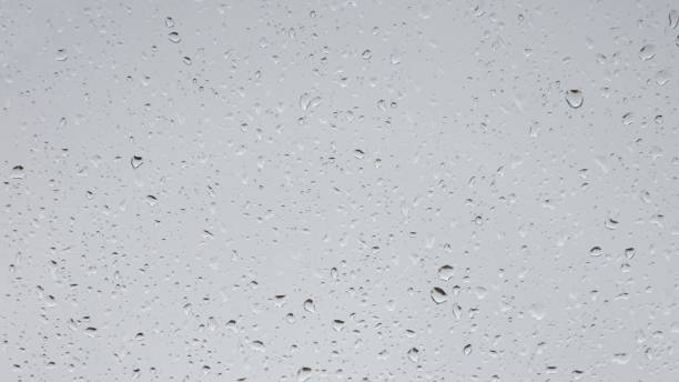 istock Wet with water drops glass window with light grey rainy background, closeup. 1289254195