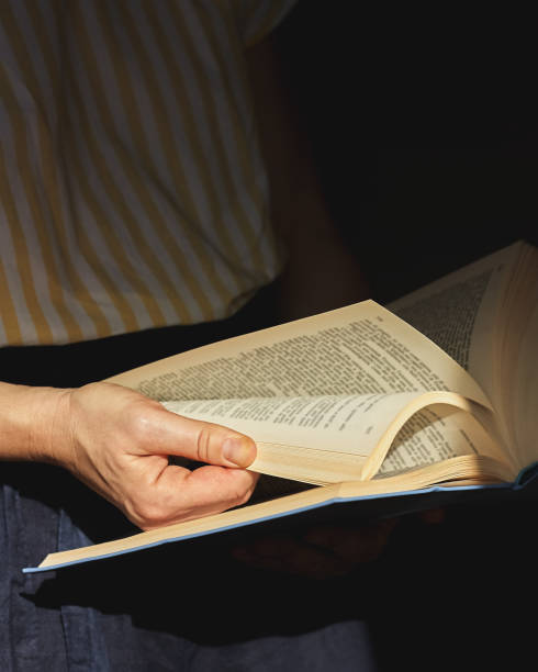 istock Woman hands leaf through a book. Shadows photography. Read and study concept. Selective focus. Toned image. 1289254969