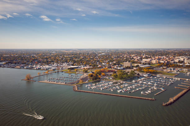 Incredible aerial city skyline wide angle panorama photograph of Sandusky, Ohio from the shoreline of the bay in Lake Erie with parks and harbors seen below on a sunny day as a boat passes by. stock photo