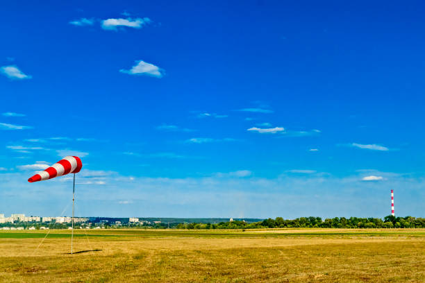 Red and white windsock wind sock on blue sky, green field and clouds background on aerodrome or airdrome. Shows wind speed and direction.