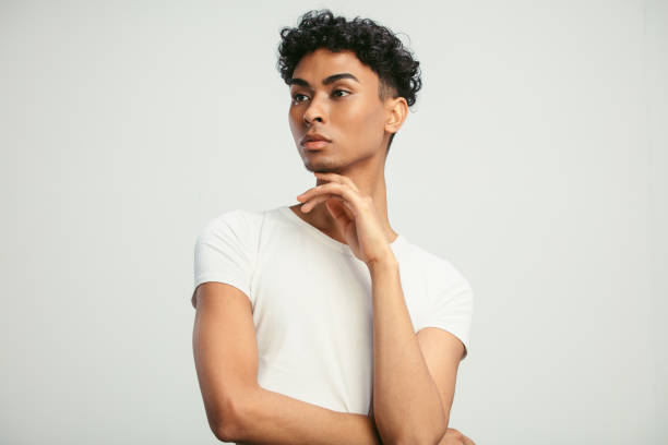 Man with feminine looks Portrait of a young man standing with his hand on chin and looking away. Androgynous man on white background. gender fluid photos stock pictures, royalty-free photos & images