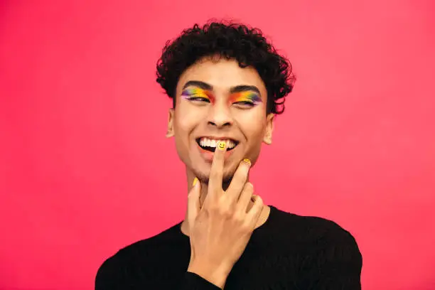 Photo of Smiling gay man with rainbow eye shadow and smiley nailpaint
