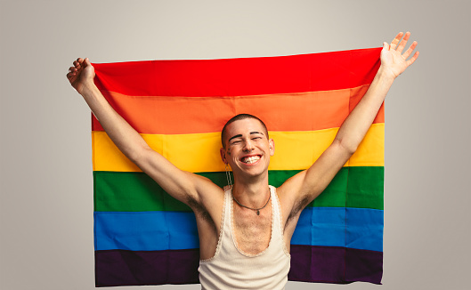 Smiling transgender man with pride flag. Cheerful man holding a lgbt flag against white background.
