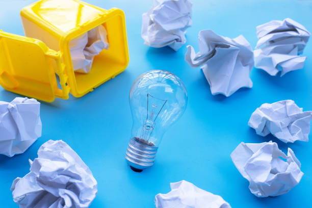 istock Yellow bin with light bulb and white crumpled paper on blue background. Ideas and creative thinking concept. Top view 1289275873