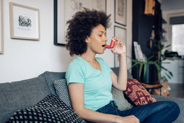 Young Afro woman using asthma inhaler at home Young African-American woman using asthma inhaler at home. asthma inhaler stock pictures, royalty-free photos & images