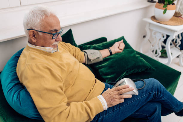 старший человек измерения кровяного давления, сидя дома - blood pressure gauge surveillance home interior house стоковые фото и изображения