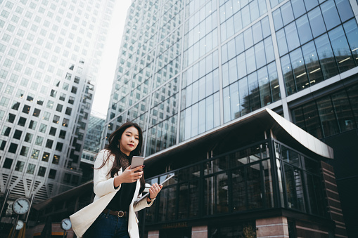 Smart Asian businesswoman managing her business with her smartphone in a financial area of the city.