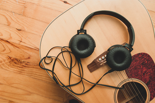 Black wired on-ear headphones and an acoustic guitar on wooden floor