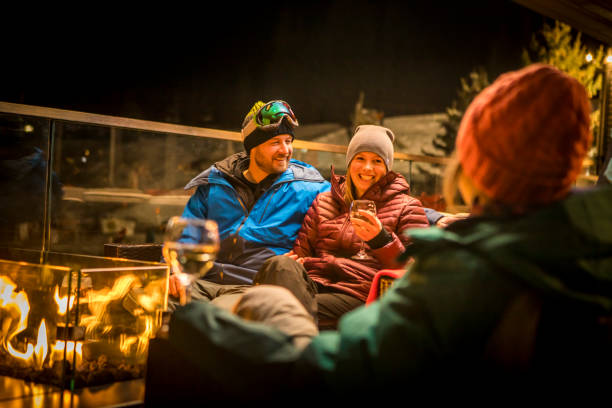 Friends sitting by fire at ski apres at night. Friends enjoying drinks by fire at outdoor patio in a pub apres ski stock pictures, royalty-free photos & images