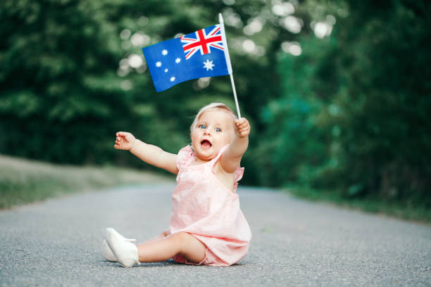 cute adorable caucasian baby girl waving australian flag. smiling child sitting on street road in park celebrating australia day holiday. celebration of national australia day in january outdoors. - australia australia day celebration flag imagens e fotografias de stock