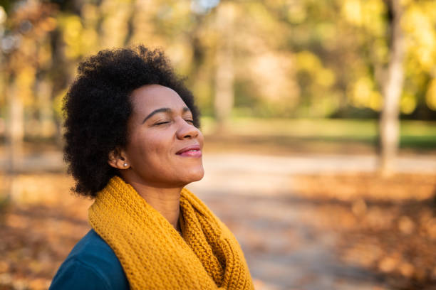 African American woman day dreaming in public park on beautiful autumn day. Happy mid adult African American woman enjoying a walk on autumn day in the park. Close up of tranquil woman inhaling and relaxing at the park. peace park stock pictures, royalty-free photos & images