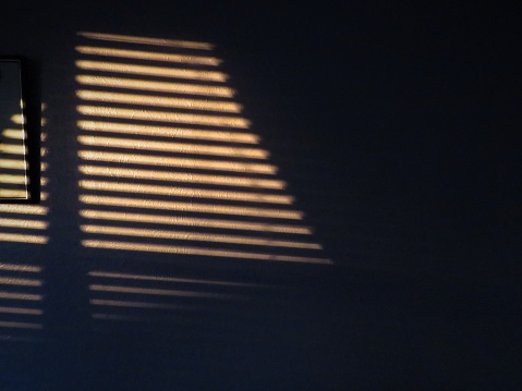 Sunset light through slatted blinds create shadows on a wall. Noir look.