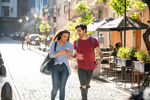 Close-up of young Hispanic couple in their 20s checking smart phone for sightseeing ideas on cobblestone side street in sunny Buenos Aires.