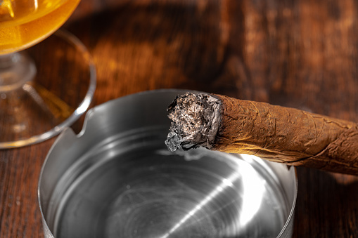 Glass of whisky and lighted cigar in an ash tray on wooden background