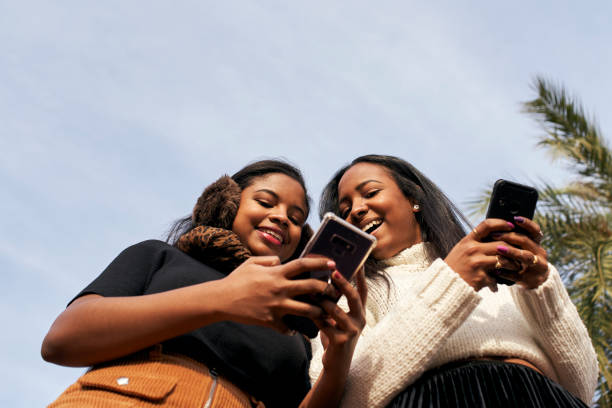 istock Low angle of two black girls using a mobile phone and laughing. People and technology concept with smartphone. 1289294094