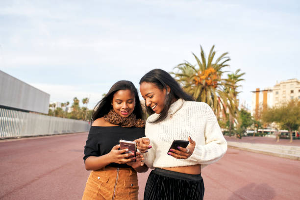 istock Two black girls walking in a city while using a mobile phone and laughing. People and technology concept with smartphone. 1289294713